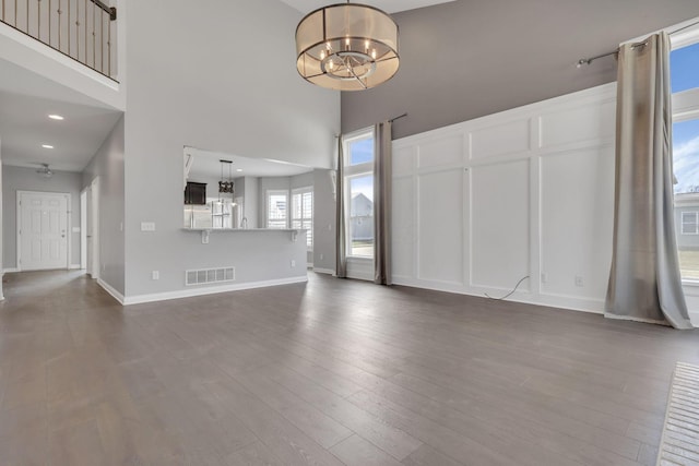 unfurnished living room with an inviting chandelier, baseboards, dark wood-style floors, and visible vents