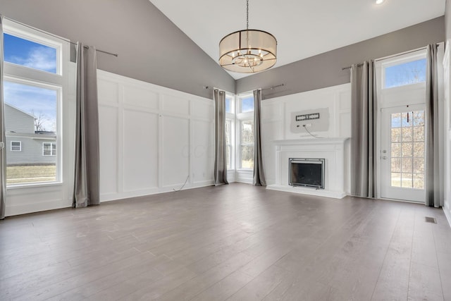 unfurnished living room with a fireplace with raised hearth, a decorative wall, vaulted ceiling, wood finished floors, and a chandelier