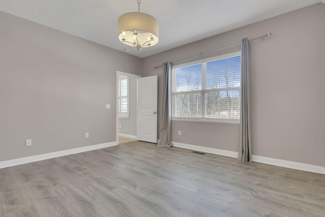 empty room with a chandelier, wood finished floors, visible vents, and baseboards