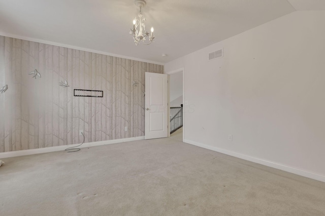 carpeted empty room featuring a notable chandelier, visible vents, baseboards, vaulted ceiling, and ornamental molding