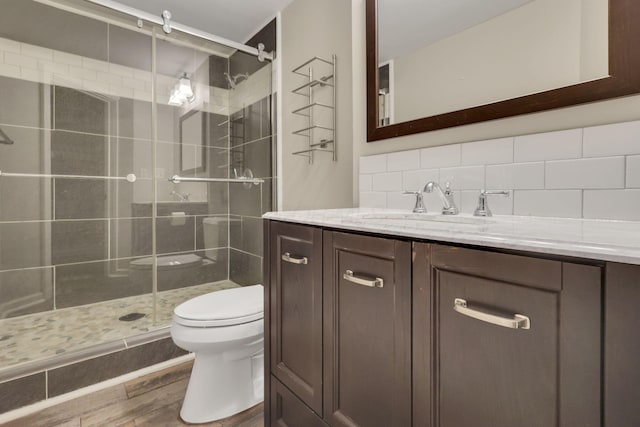 bathroom featuring a stall shower, decorative backsplash, toilet, wood finished floors, and vanity