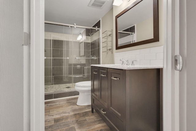 full bathroom featuring a stall shower, backsplash, toilet, and wood finished floors