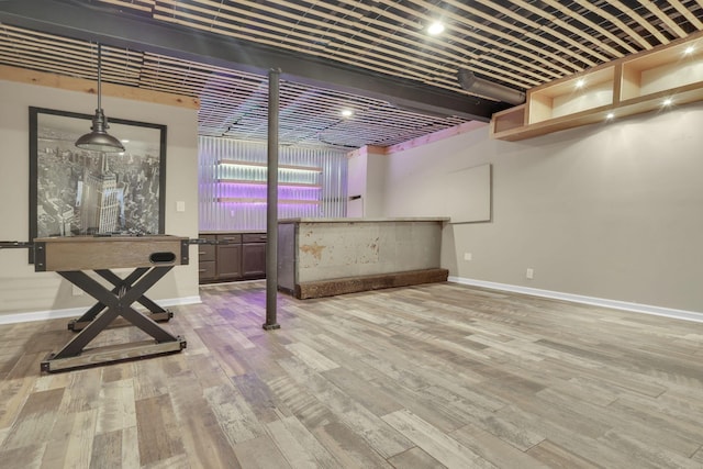 below grade area featuring a bar, baseboards, and wood finished floors