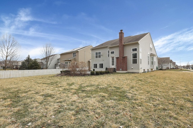 rear view of house with a chimney, fence, and a yard