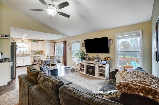 living area featuring a wealth of natural light, dark wood-style flooring, a glass covered fireplace, and vaulted ceiling