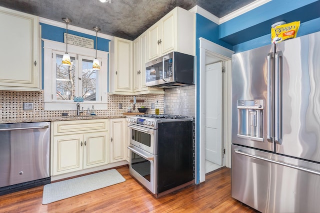 kitchen featuring light wood-style flooring, appliances with stainless steel finishes, light stone counters, cream cabinetry, and a sink