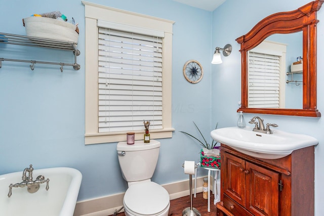 full bath featuring baseboards, toilet, wood finished floors, a freestanding bath, and vanity