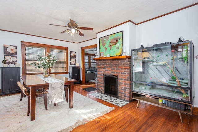 dining area with a textured ceiling, a fireplace, wood finished floors, a ceiling fan, and crown molding