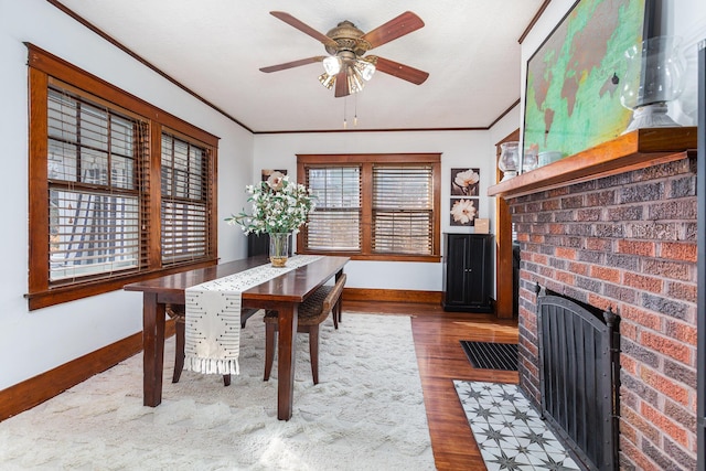 dining area with a brick fireplace, baseboards, ornamental molding, and wood finished floors