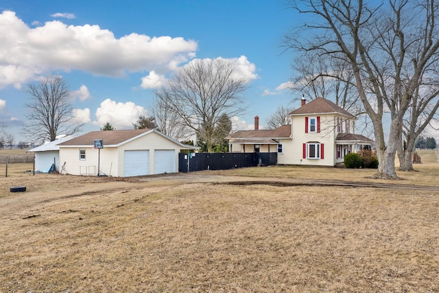 view of front of home with a chimney, a detached garage, fence, and a front yard