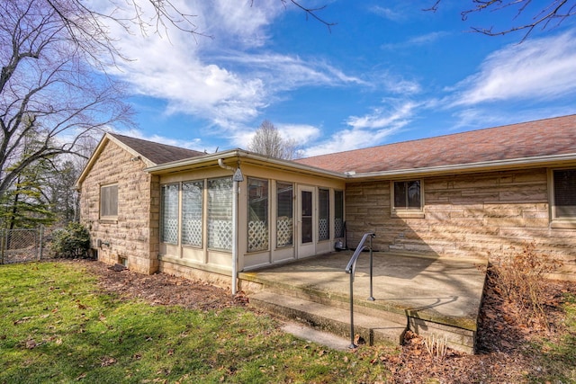 back of property featuring a patio, fence, a sunroom, stone siding, and roof with shingles