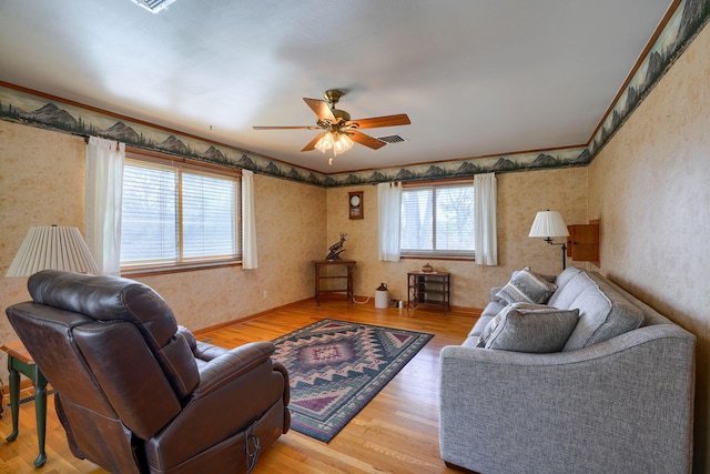 living room with crown molding, wood finished floors, visible vents, a ceiling fan, and wallpapered walls