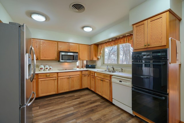 kitchen with stainless steel appliances, a sink, visible vents, light countertops, and dark wood-style floors