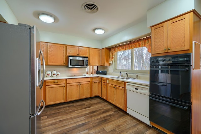 kitchen with dark wood-style floors, stainless steel appliances, light countertops, visible vents, and a sink