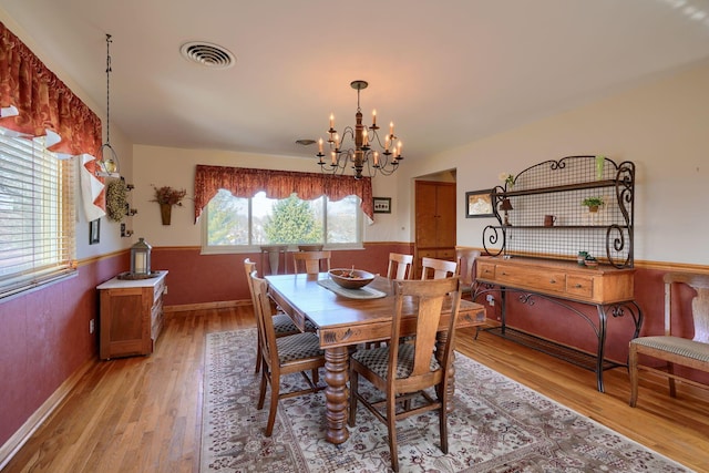 dining area with a wainscoted wall, an inviting chandelier, visible vents, and light wood-style floors