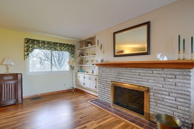 living room with a brick fireplace, wood finished floors, visible vents, and baseboards