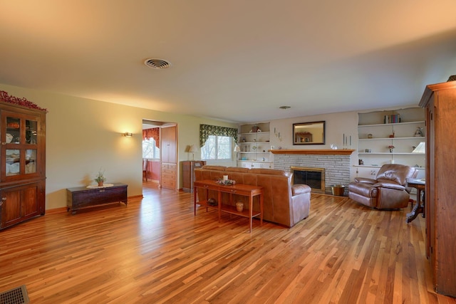 living area with light wood-type flooring, a fireplace, and visible vents