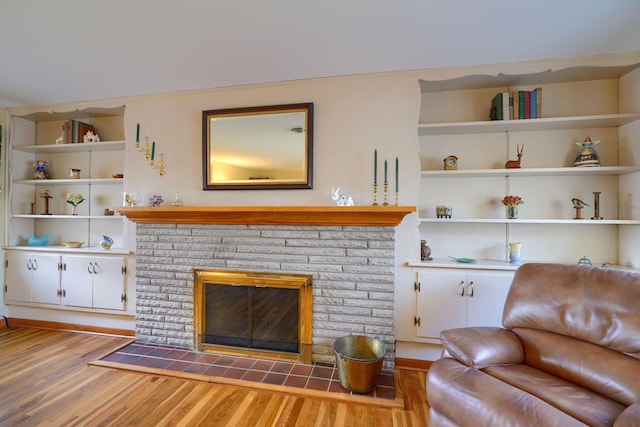 living room with built in shelves, a fireplace, and wood finished floors