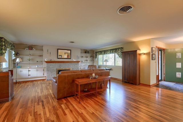 living room with a brick fireplace, light wood-style flooring, visible vents, and baseboards