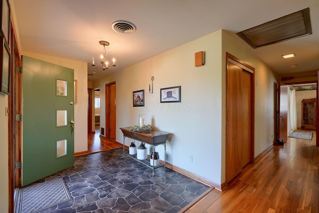 foyer featuring an inviting chandelier, stone finish flooring, visible vents, and baseboards