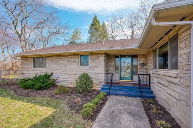 entrance to property with stone siding, a shingled roof, and fence