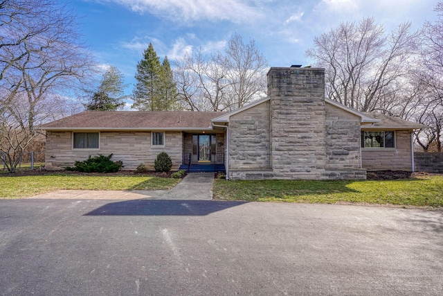 view of front of home featuring stone siding, a front lawn, a chimney, and a shingled roof