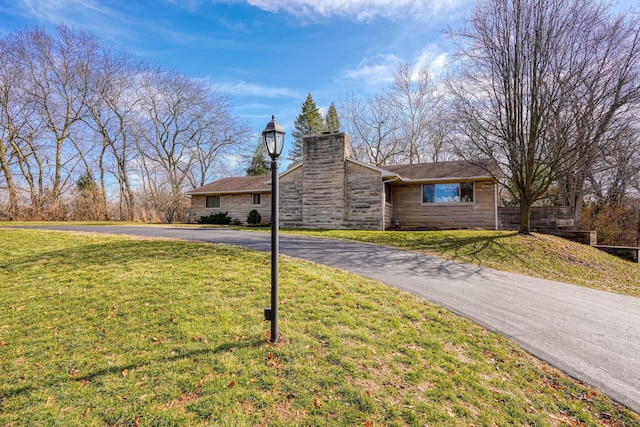 ranch-style house featuring stone siding, aphalt driveway, a front lawn, and a chimney