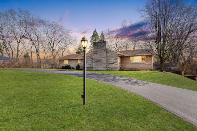 view of front of house with stone siding, a chimney, aphalt driveway, and a lawn