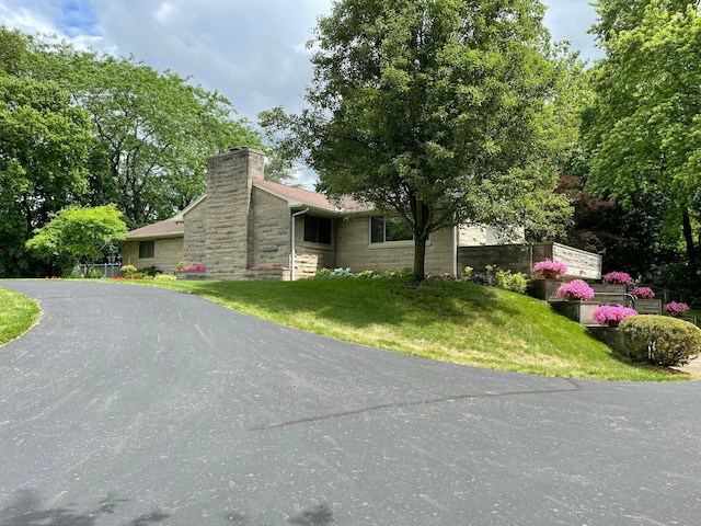 view of front facade featuring a front yard, stone siding, and a chimney