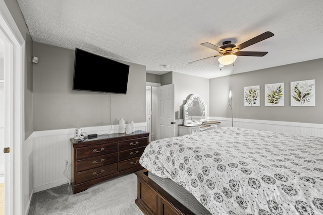 bedroom with light carpet, a wainscoted wall, a ceiling fan, and a textured ceiling