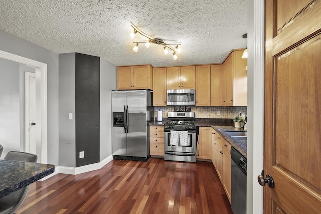 kitchen featuring dark wood finished floors, dark countertops, a sink, stainless steel appliances, and backsplash