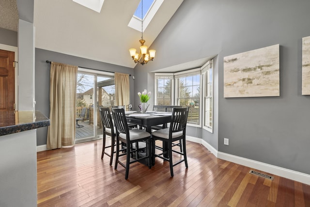 dining area with a skylight, high vaulted ceiling, hardwood / wood-style floors, a chandelier, and baseboards