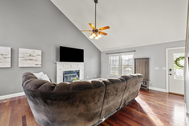 living room with high vaulted ceiling, dark wood-style flooring, a glass covered fireplace, and baseboards