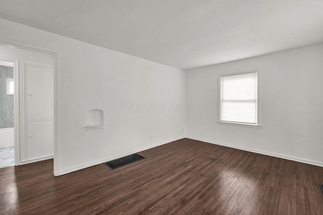 empty room with baseboards, visible vents, and dark wood finished floors