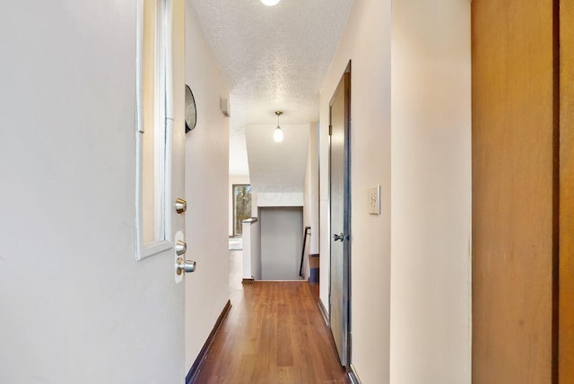 hall featuring a textured ceiling, wood finished floors, and baseboards