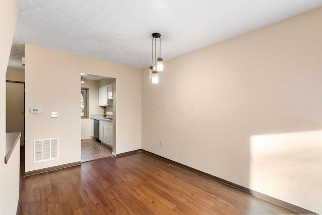 unfurnished room featuring visible vents, a textured ceiling, baseboards, and wood finished floors