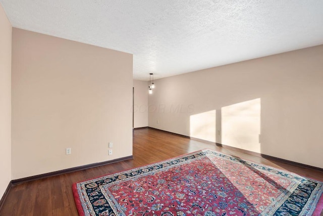 empty room featuring a textured ceiling, baseboards, and wood finished floors