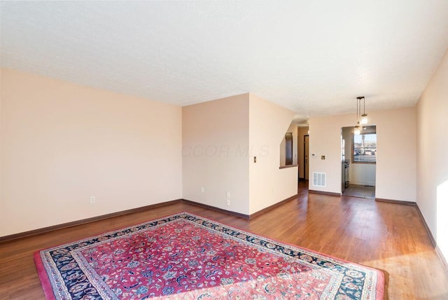 empty room with wood finished floors, visible vents, and baseboards