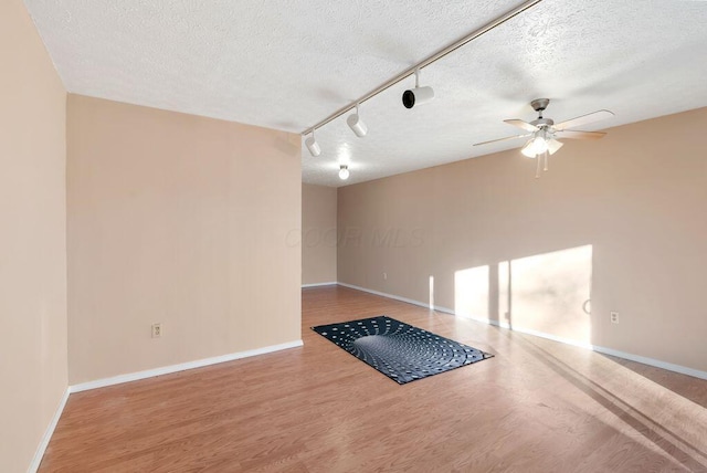 empty room with a ceiling fan, a textured ceiling, track lighting, wood finished floors, and baseboards