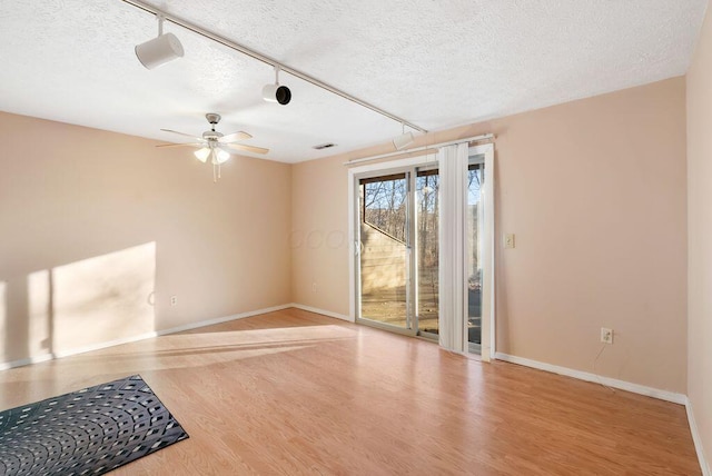 interior space with rail lighting, a textured ceiling, baseboards, and wood finished floors