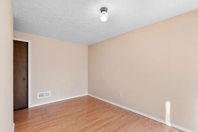 spare room featuring a textured ceiling, light wood-style flooring, visible vents, and baseboards