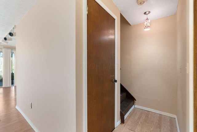 corridor with light wood-style flooring, baseboards, and a textured ceiling