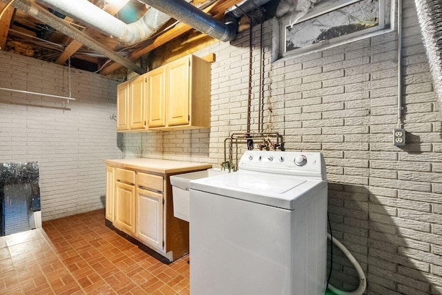 clothes washing area with washer / dryer, brick wall, brick floor, and cabinet space