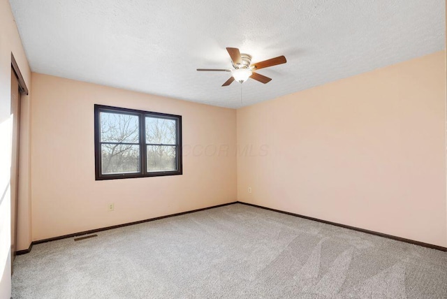 empty room featuring carpet floors, visible vents, a textured ceiling, and baseboards