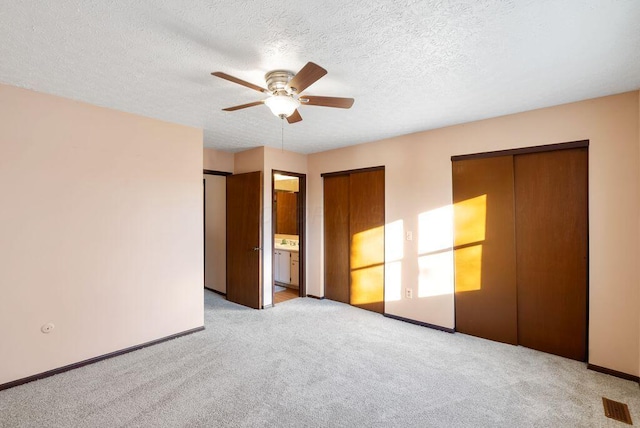 unfurnished bedroom with baseboards, a ceiling fan, light colored carpet, a textured ceiling, and multiple closets