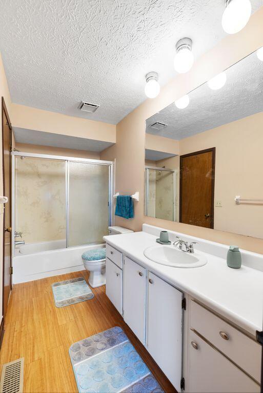 full bath with visible vents, toilet, enclosed tub / shower combo, vanity, and wood finished floors