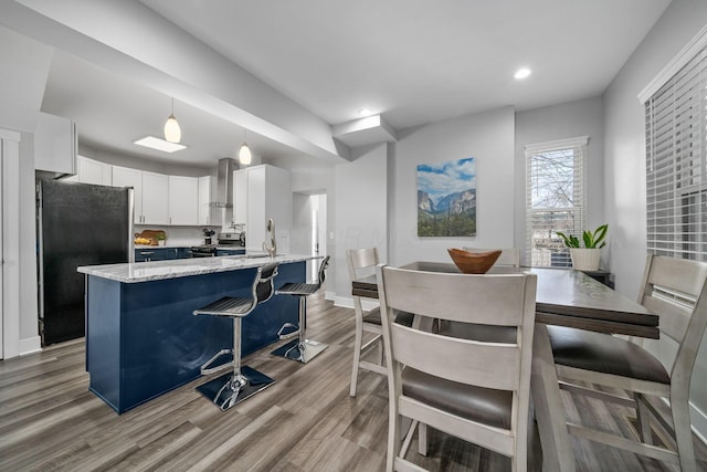 kitchen with light stone counters, wood finished floors, freestanding refrigerator, stainless steel range oven, and wall chimney exhaust hood