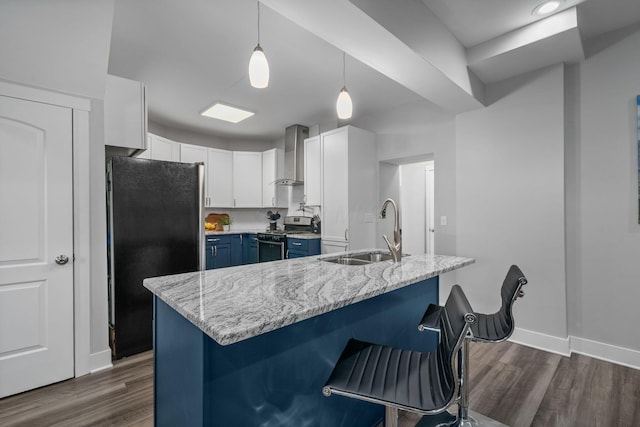 kitchen featuring stainless steel gas range, freestanding refrigerator, a sink, a kitchen breakfast bar, and wall chimney exhaust hood