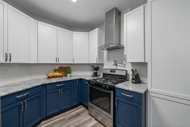 kitchen featuring stainless steel gas range oven, light wood-style flooring, blue cabinetry, tasteful backsplash, and wall chimney range hood