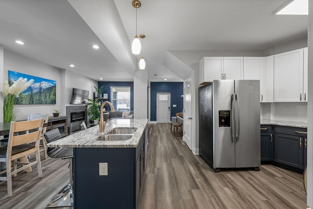 kitchen with light stone countertops, a tiled fireplace, open floor plan, stainless steel fridge with ice dispenser, and a sink